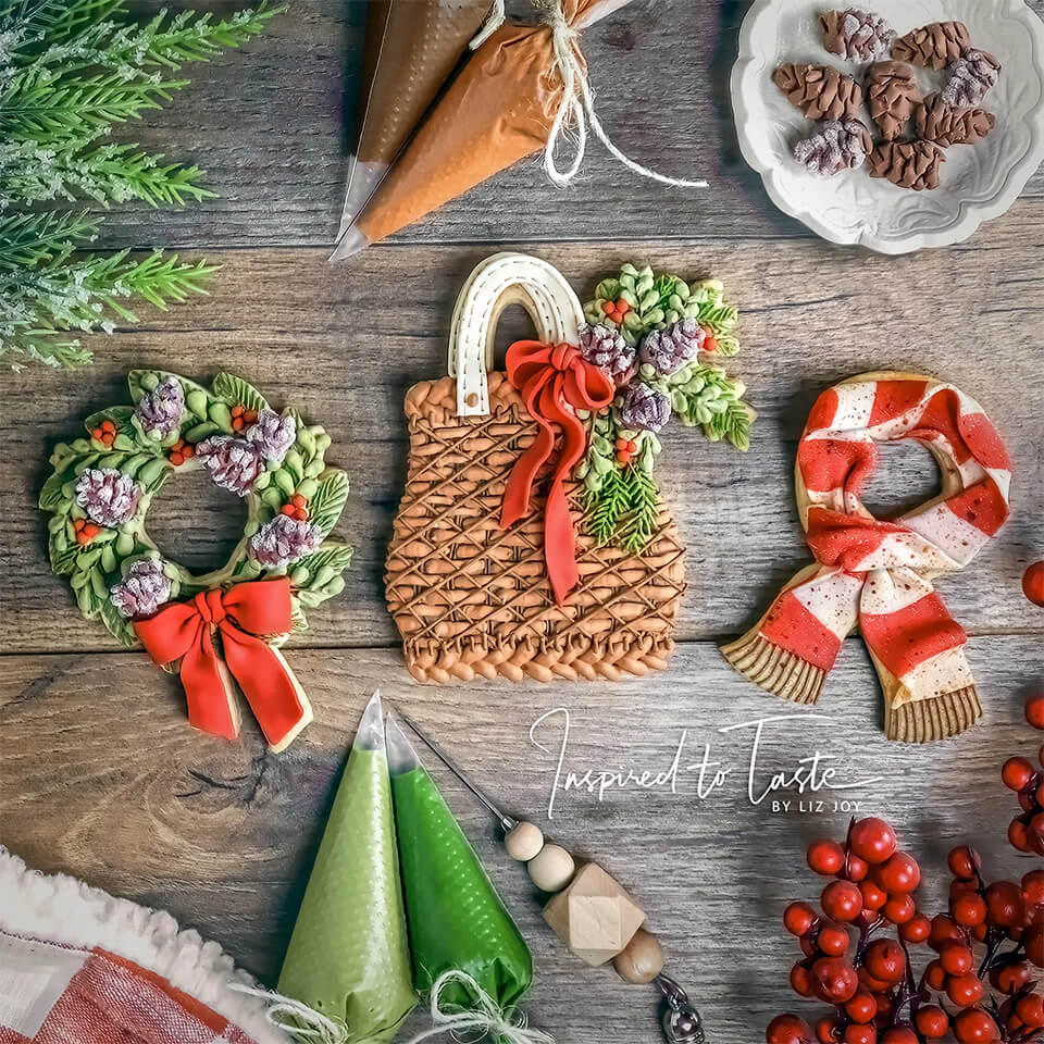 Three intricately frosted cookies in the shape of a wreath, basket and scarf