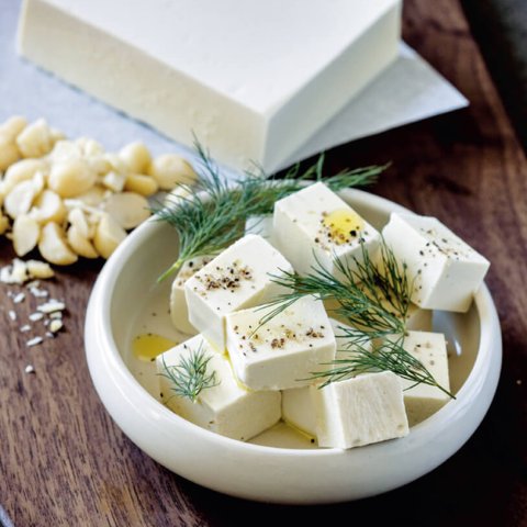 A white dish of feta cheese on a brown cutting board