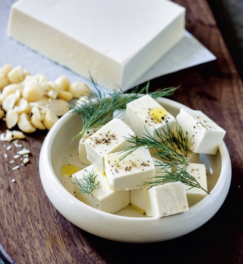A white dish of feta cheese on a brown cutting board
