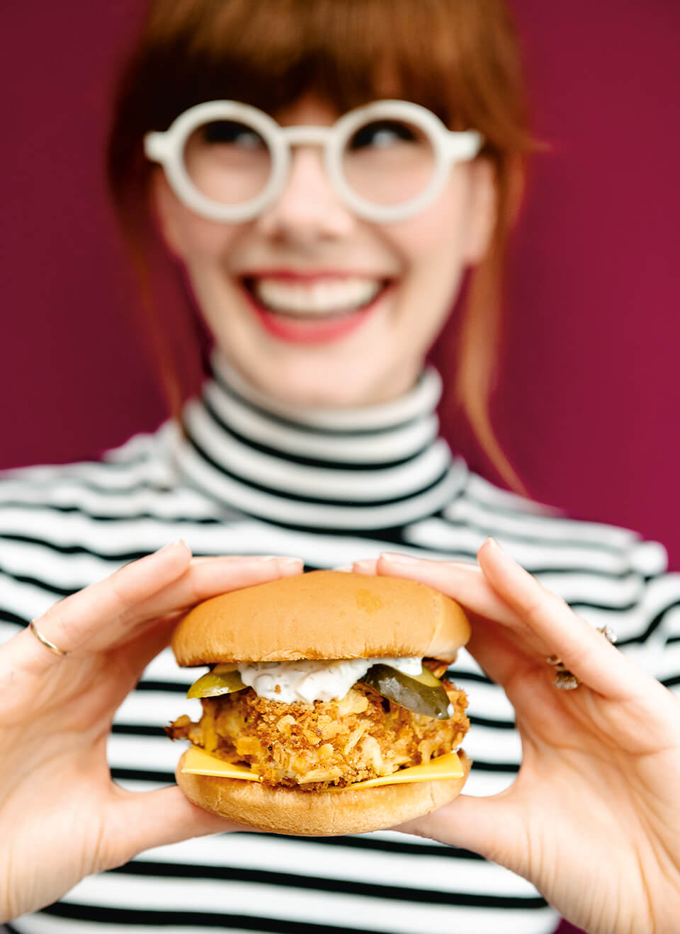 A woman, Mary Berg, holds a fried fish sandwich in front of a red background