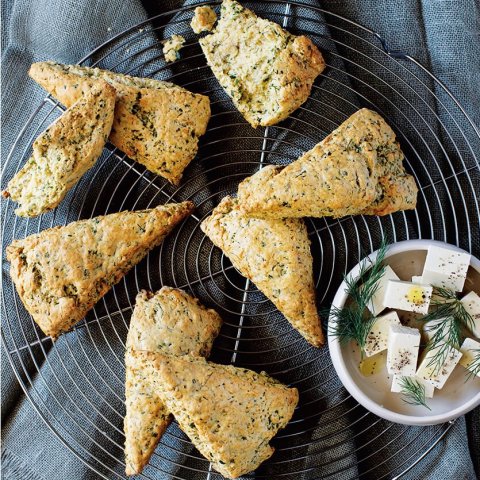 A rack of scones over a blue towel with a small white dish of feta cheese