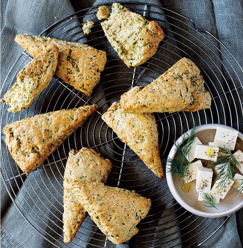 A rack of scones over a blue towel with a small white dish of feta cheese