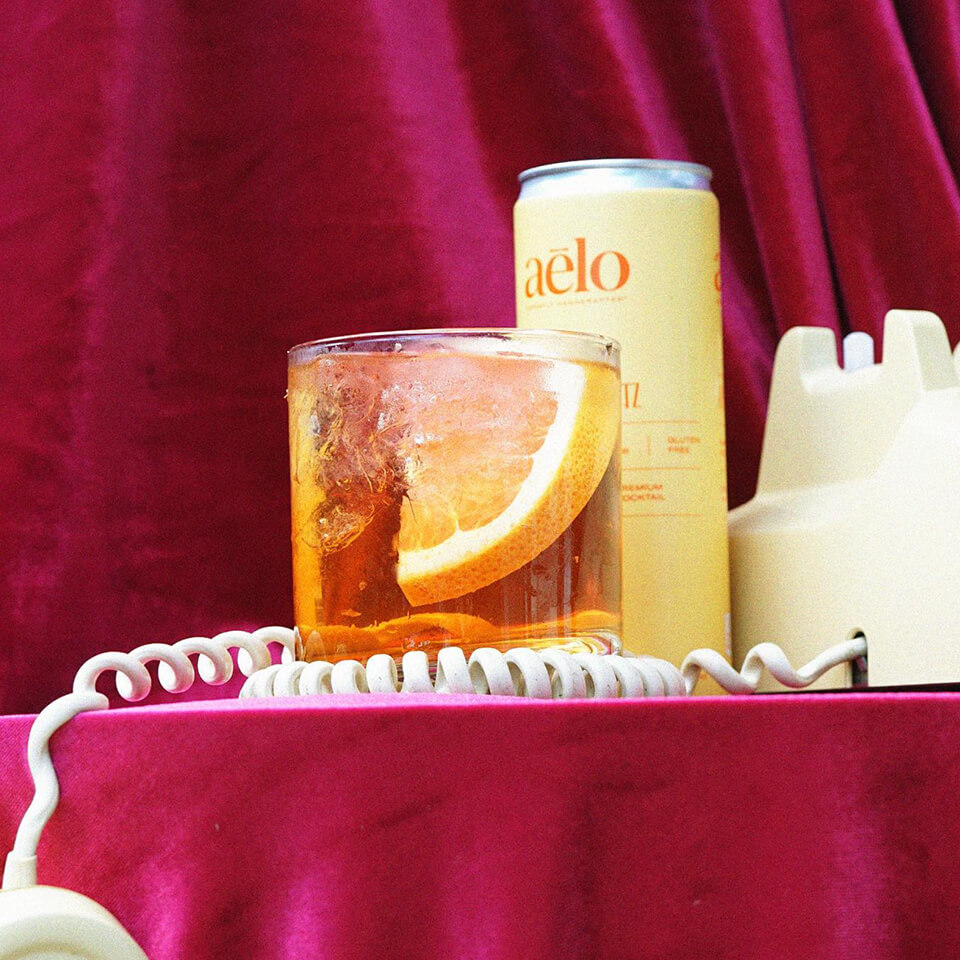 A yellow can, a cocktail and a white telephone against a pink velvet background