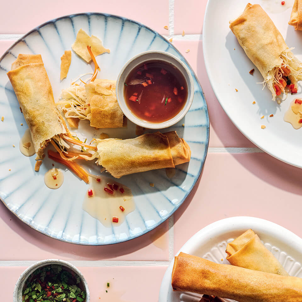 Spring rolls with dipping sauces on a plate on a pink surfave