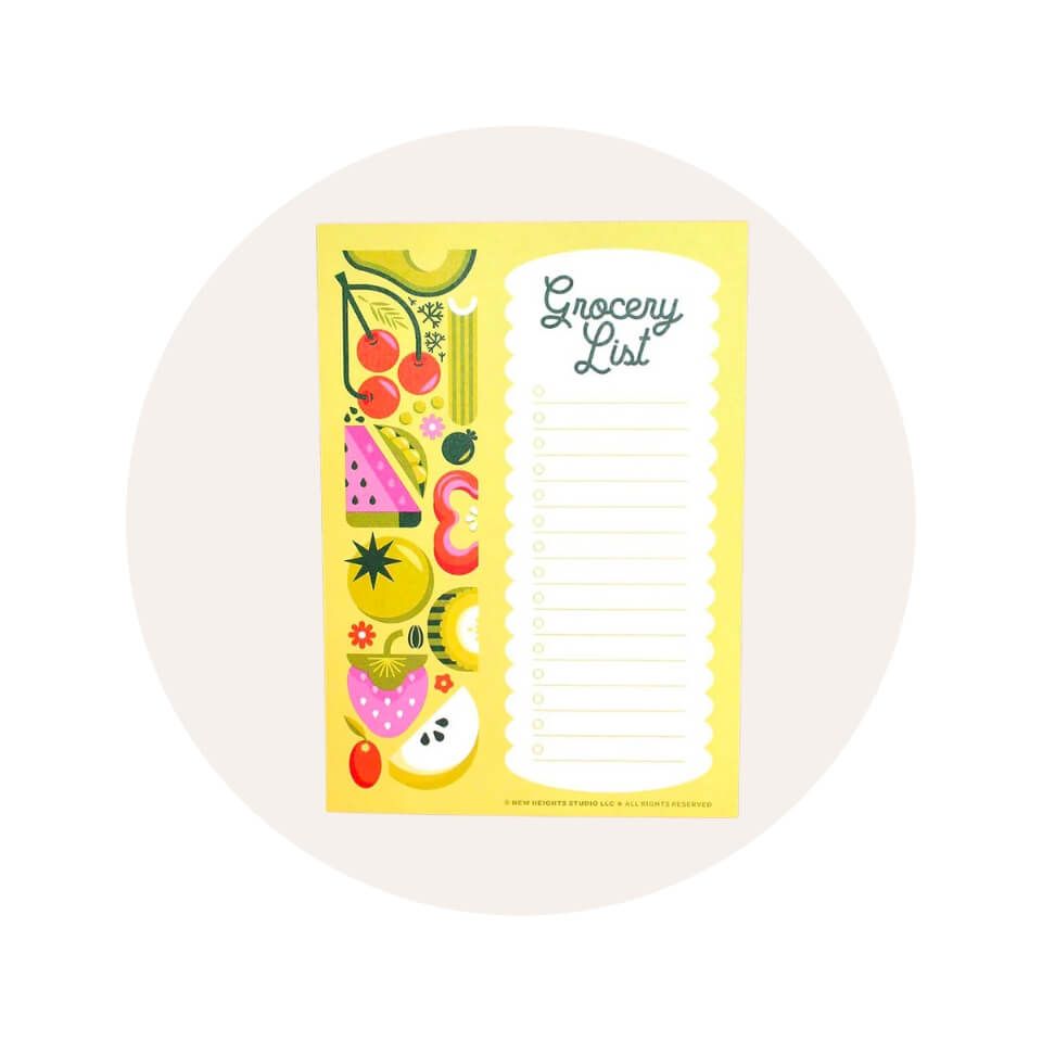 A neon yellow pad with the words "Grocery List" written in dark green cursive and a fruit-vegetable pattern in a cream-coloured circle