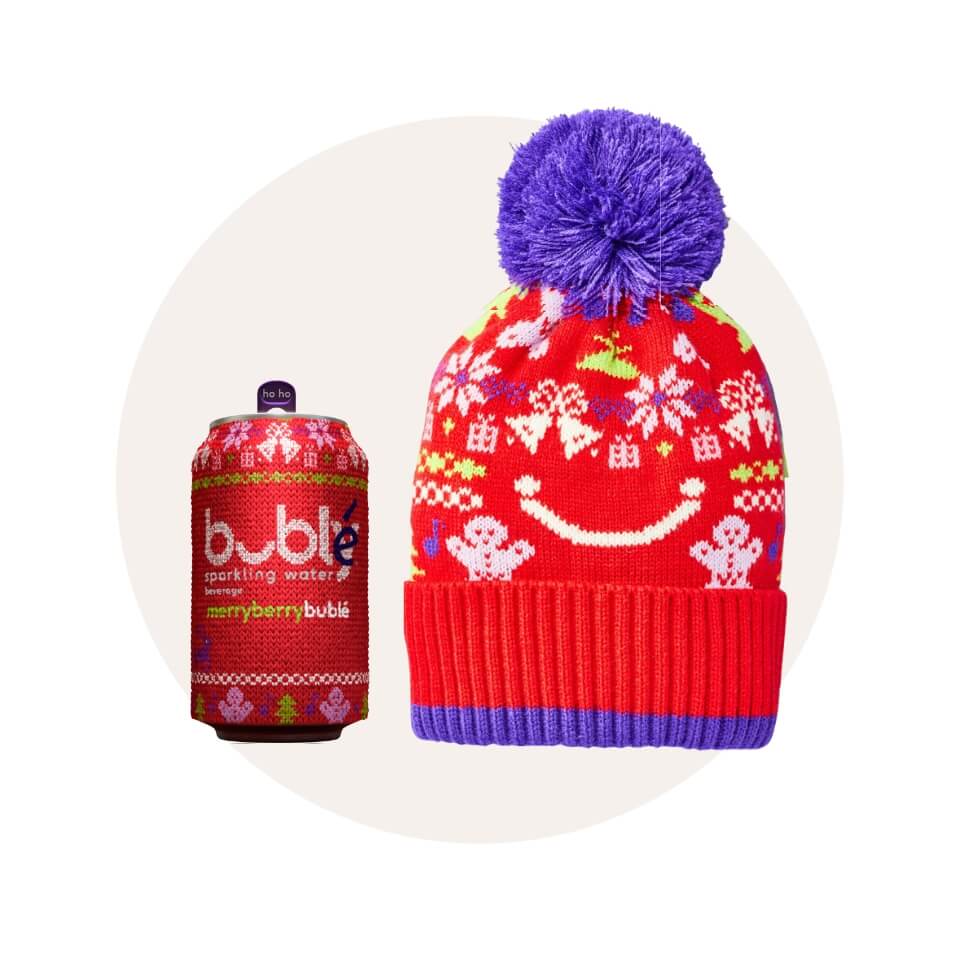 A red patterned hat with a purple pom-pom and matching soda can in front of a cream-coloured circle