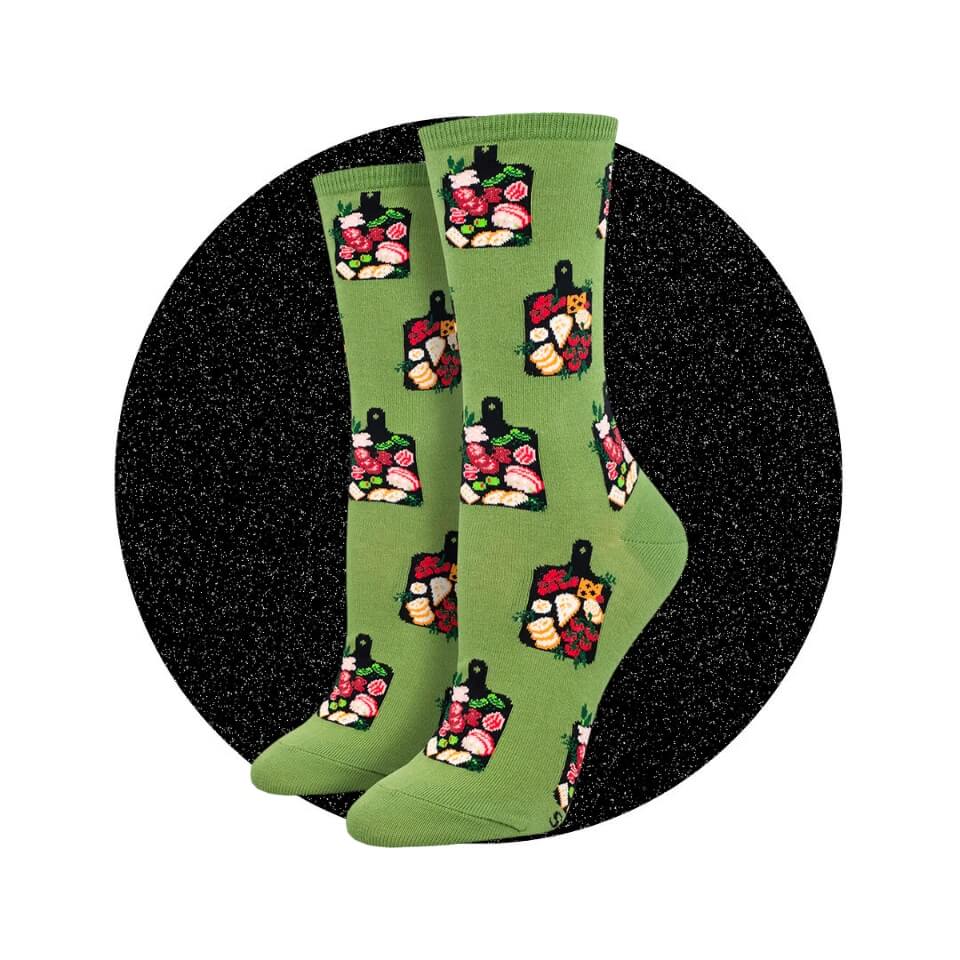 A pair of light green socks with illustrations of charcuterie and cheese boards over a sparkly black circle