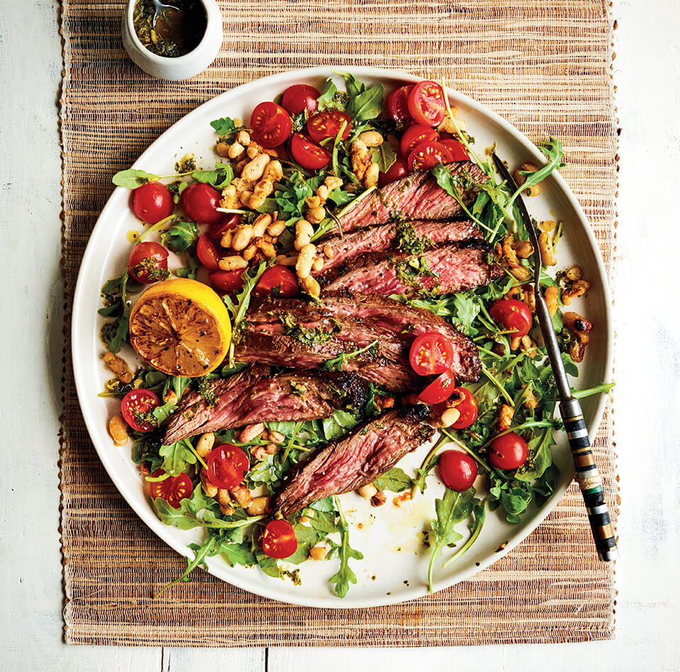 A white plate with salad and sliced steak on a woven placemat