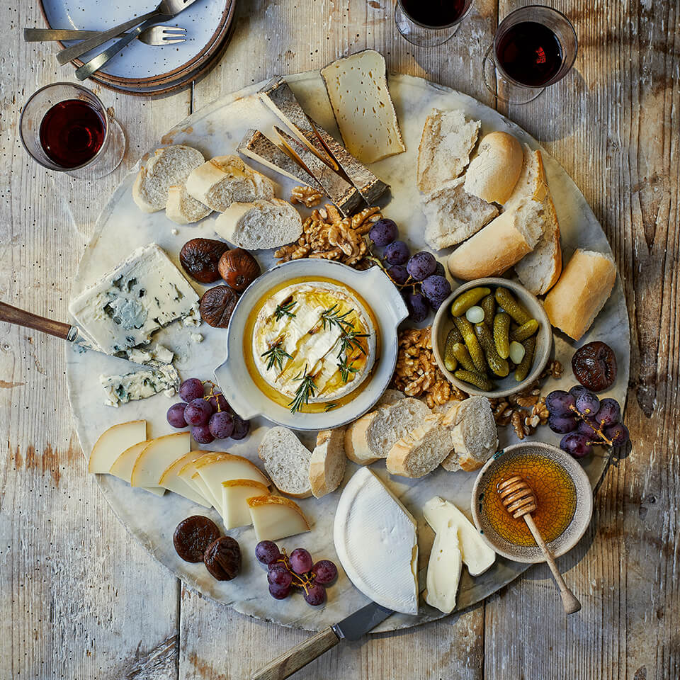 A wooden grazing board with various cheeses and ramekins