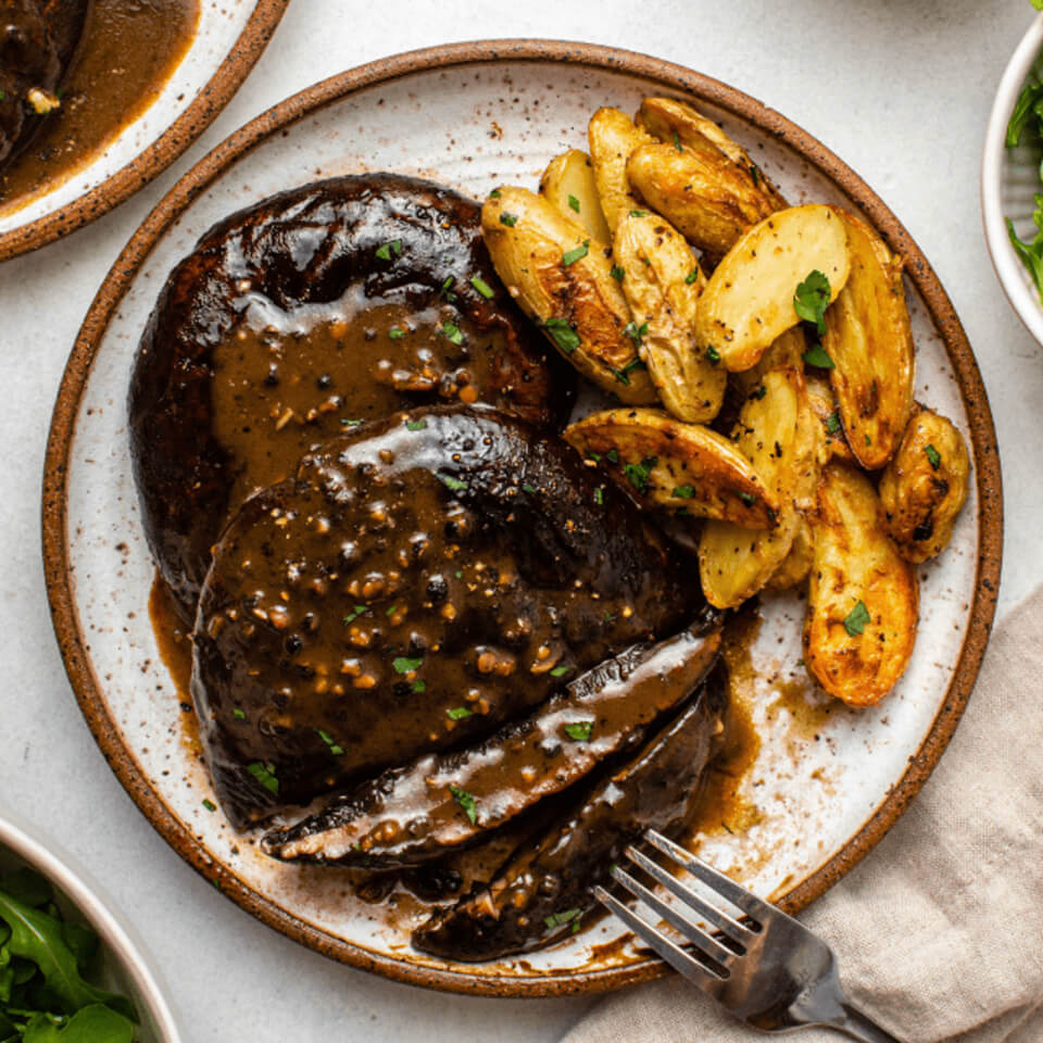 A plate with portobello mushroom steaks and potato wedges
