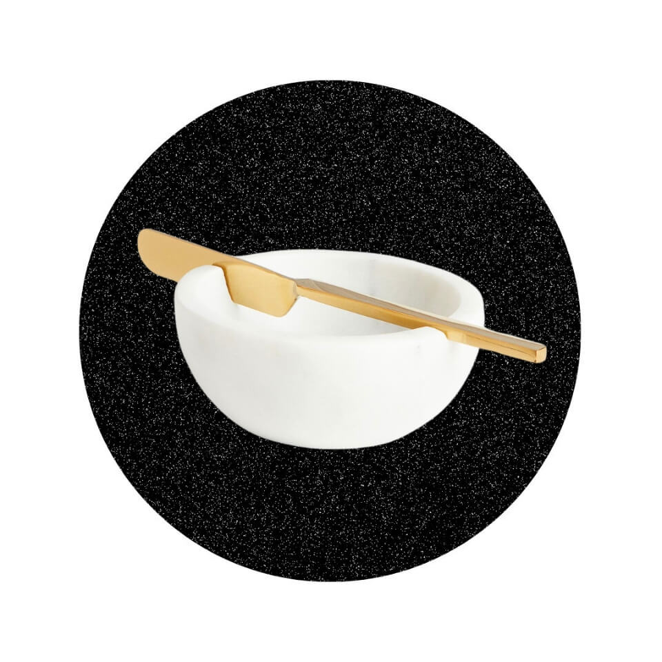 A white marble bowl with a gold butter knife slotted into the top in a sparkly black circle