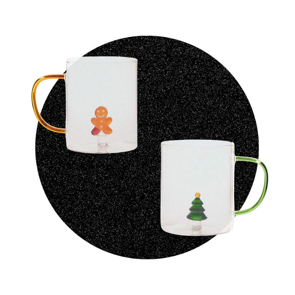 Two glass mugs with Christmas figurines over a sparkly black circle