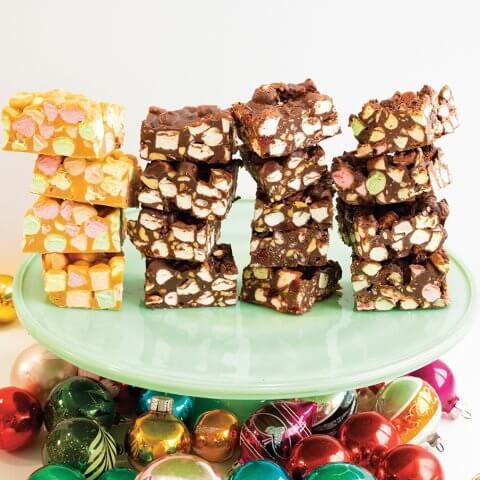 Stacks of marshmallow cookie bars on a light green cake stand on top of multicoloured Christmas ornaments