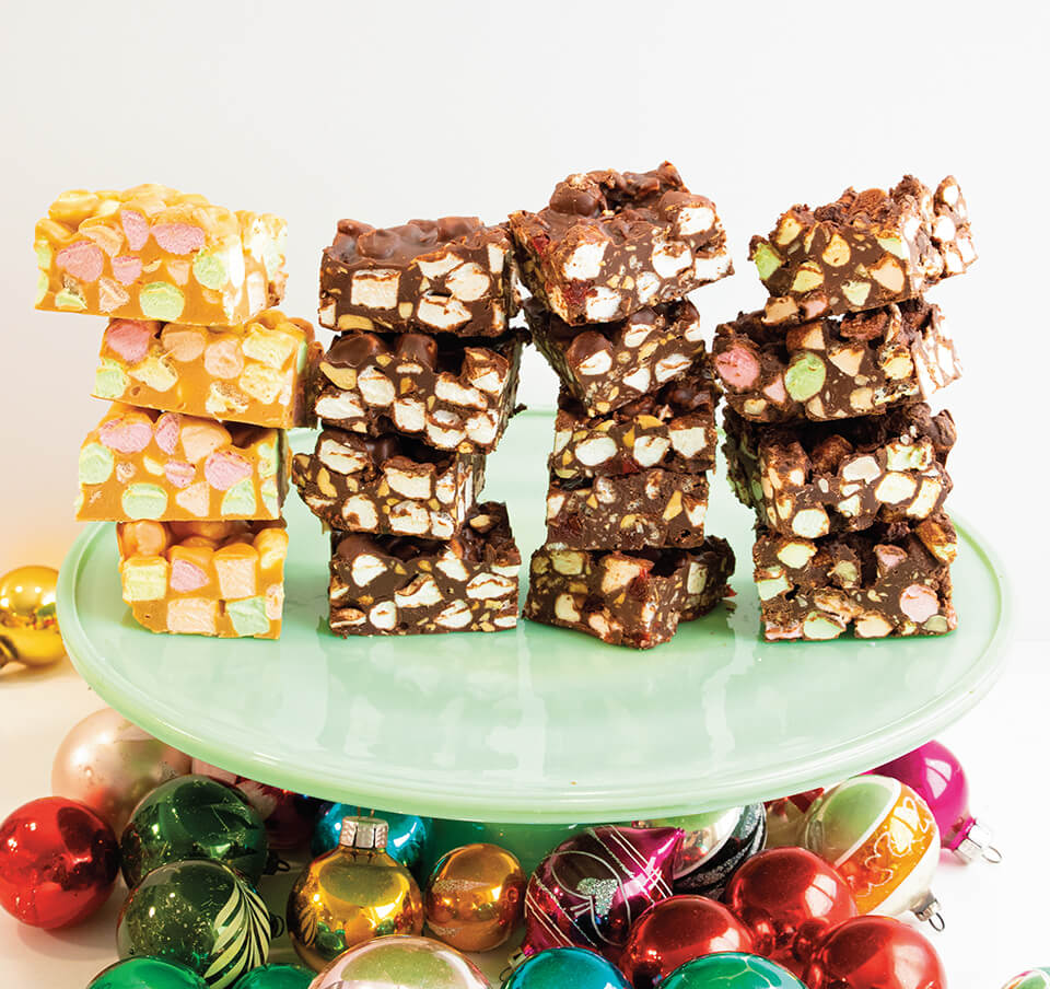 Stacks of marshmallow cookie bars on a light green cake stand on top of multicoloured Christmas ornaments