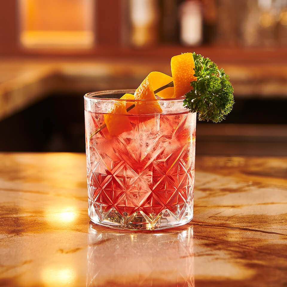A Negroni cocktail with an orange twist and parsley garnish