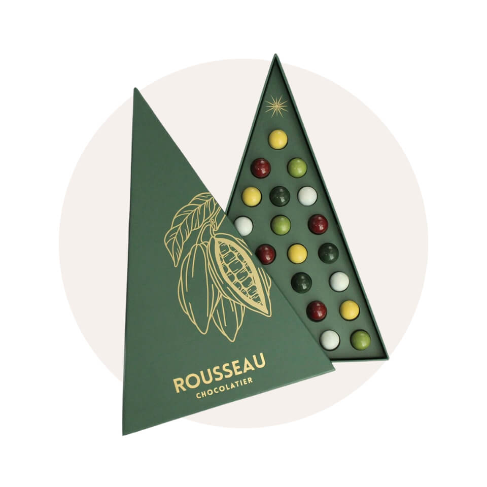 A box of chocolates shaped like a Christmas tree over a cream-coloured circle