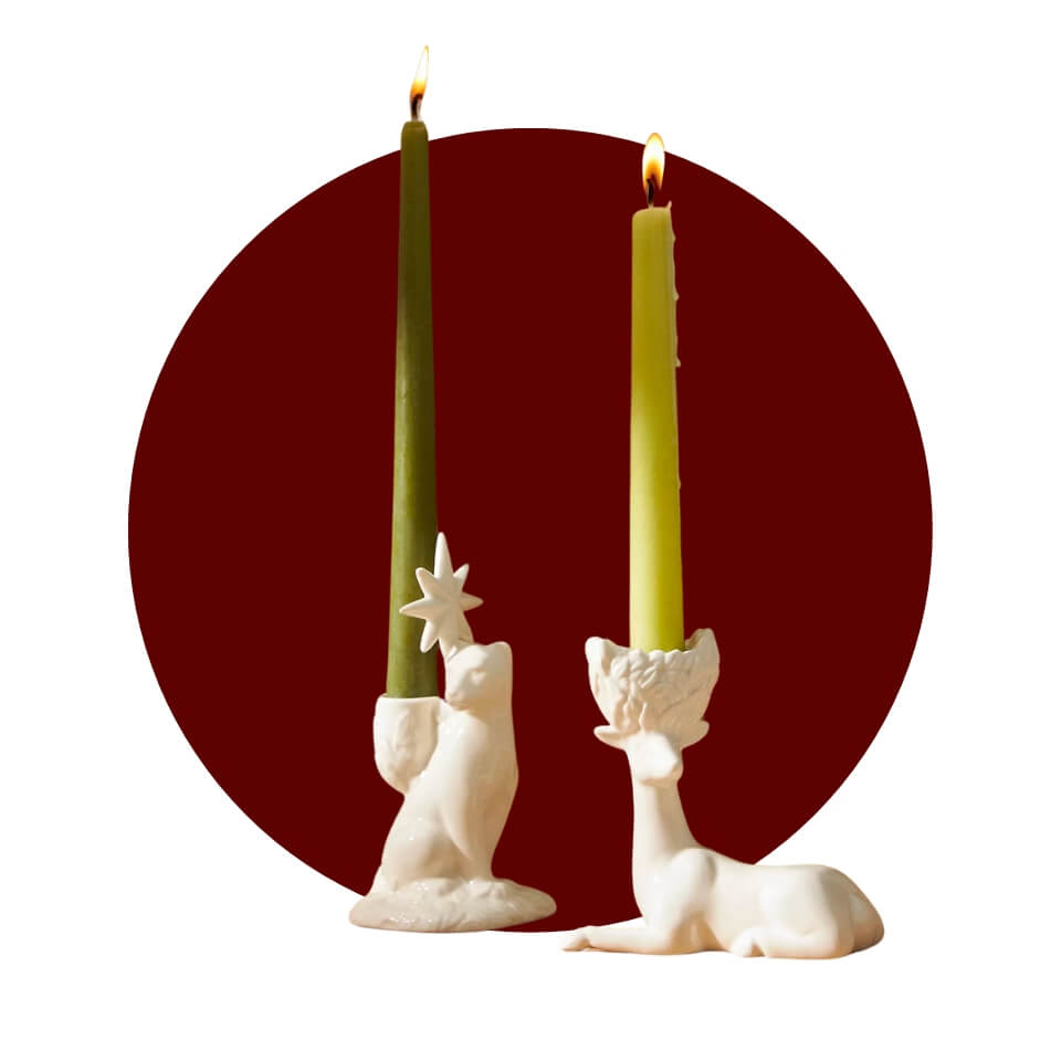Two white animal-shaped candle holders with green taper candles over a maroon circle