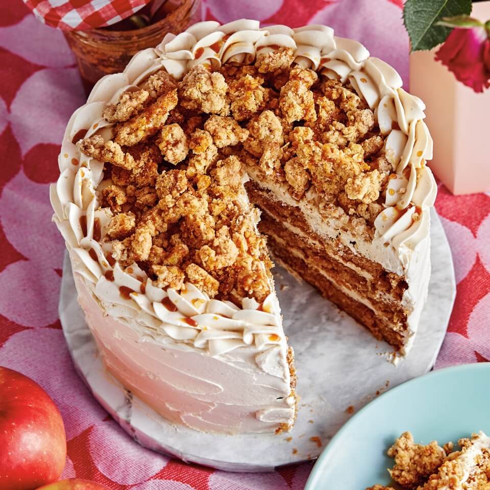 A frosted cake topped with oatmeal crumble on a pink-and-red tablecloth