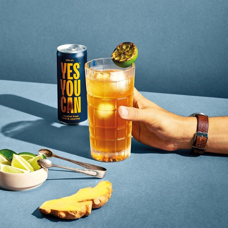 A person's hand holding a cocktail with a blue and yellow can