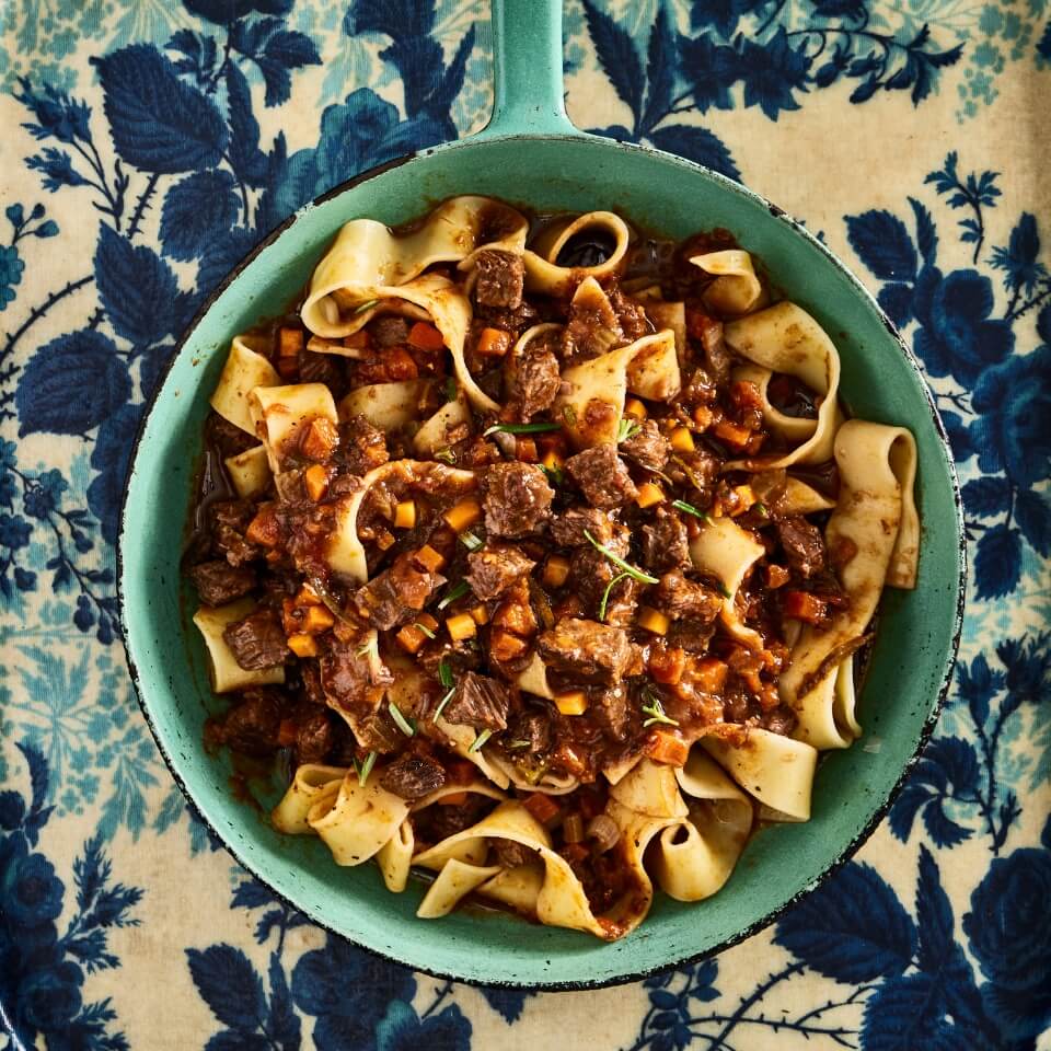 A blue skillet with pasta and short rib ragu over a toile surface