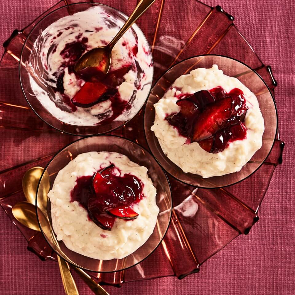 Three portions of rice pudding and gold spoons in a dish over a red-purple tablecloth
