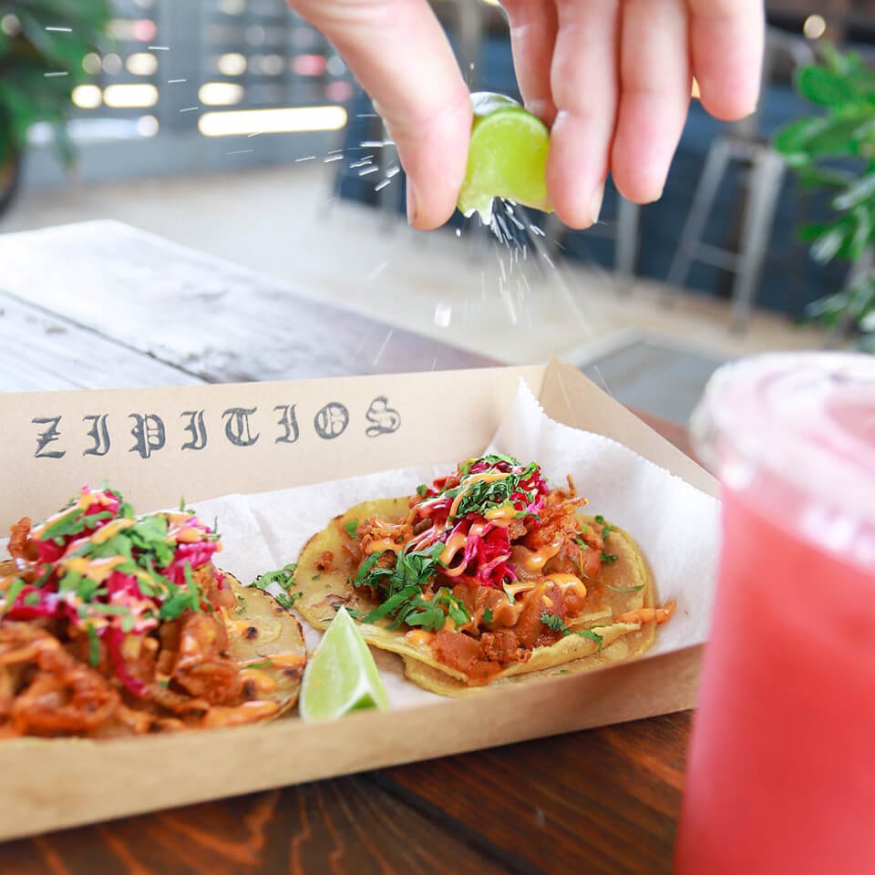 A person squeezing lime over two tacos