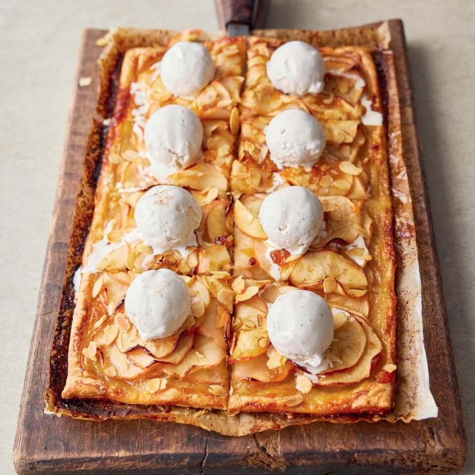 A baking tray with a sliced apple tart topped with scoops of ice cream