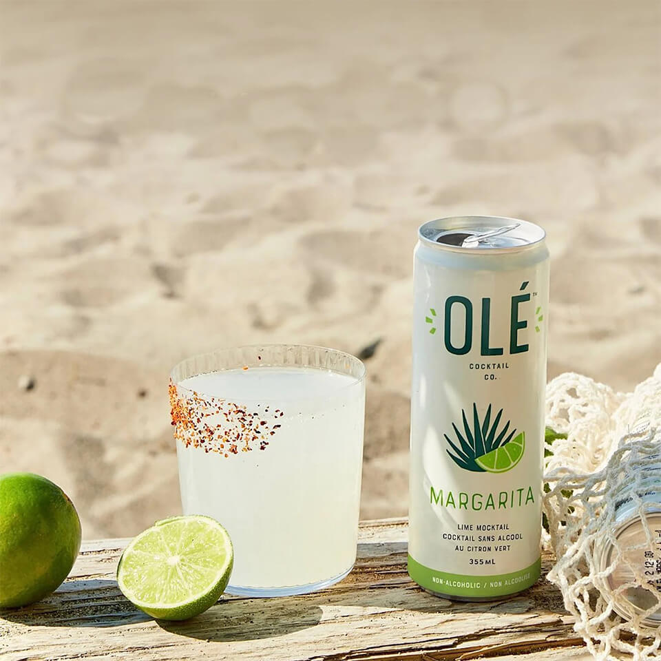 A green can and glass with margarita on a wooden bench on a beach