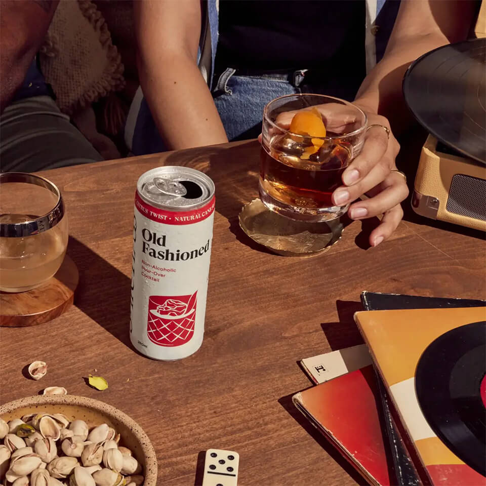 A red and white can and a person's hand holding a cocktail on top of a games table