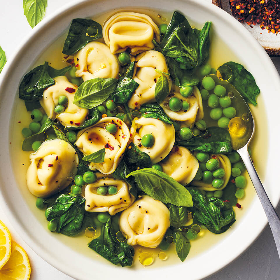 A white bowl with tortellini and green vegetable soup