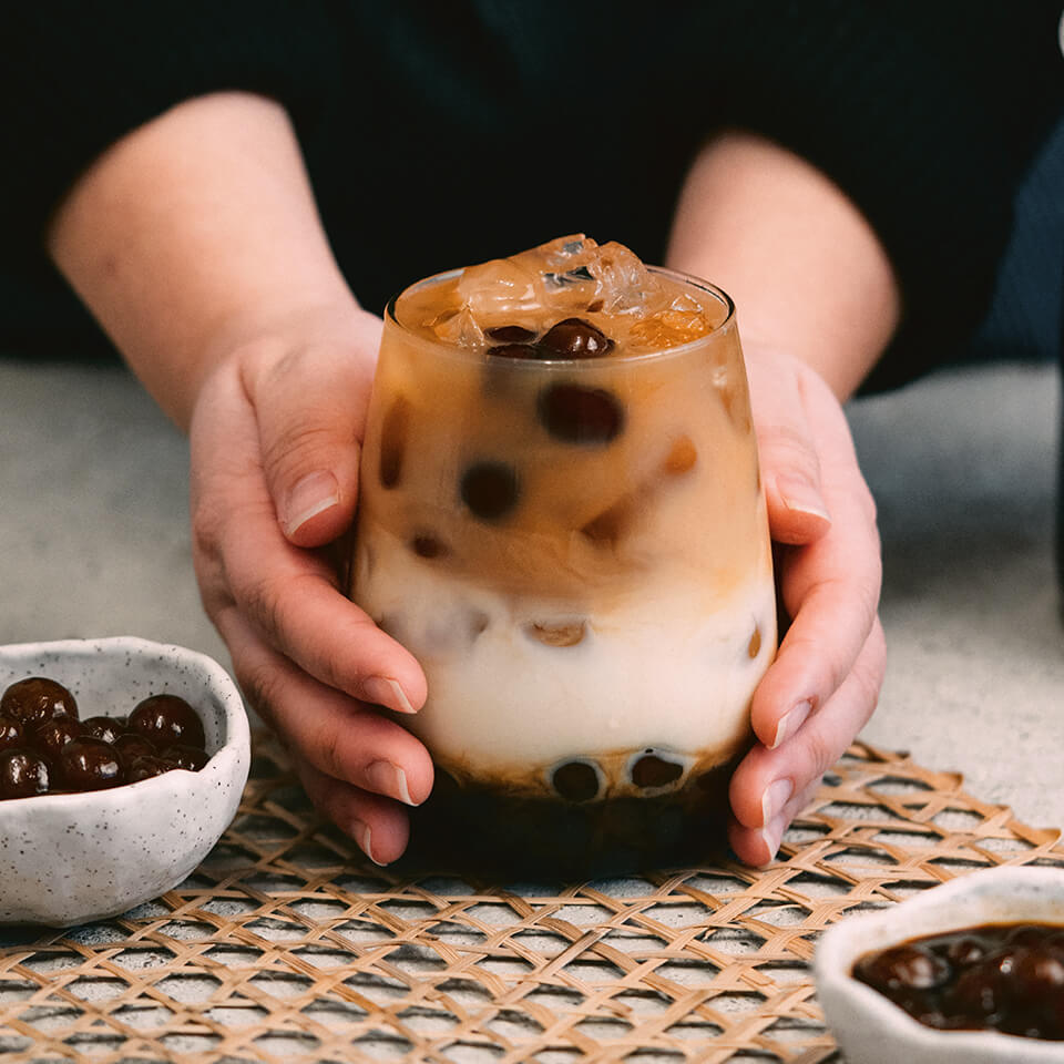 A person's hands holding a cup with layered boba milk tea