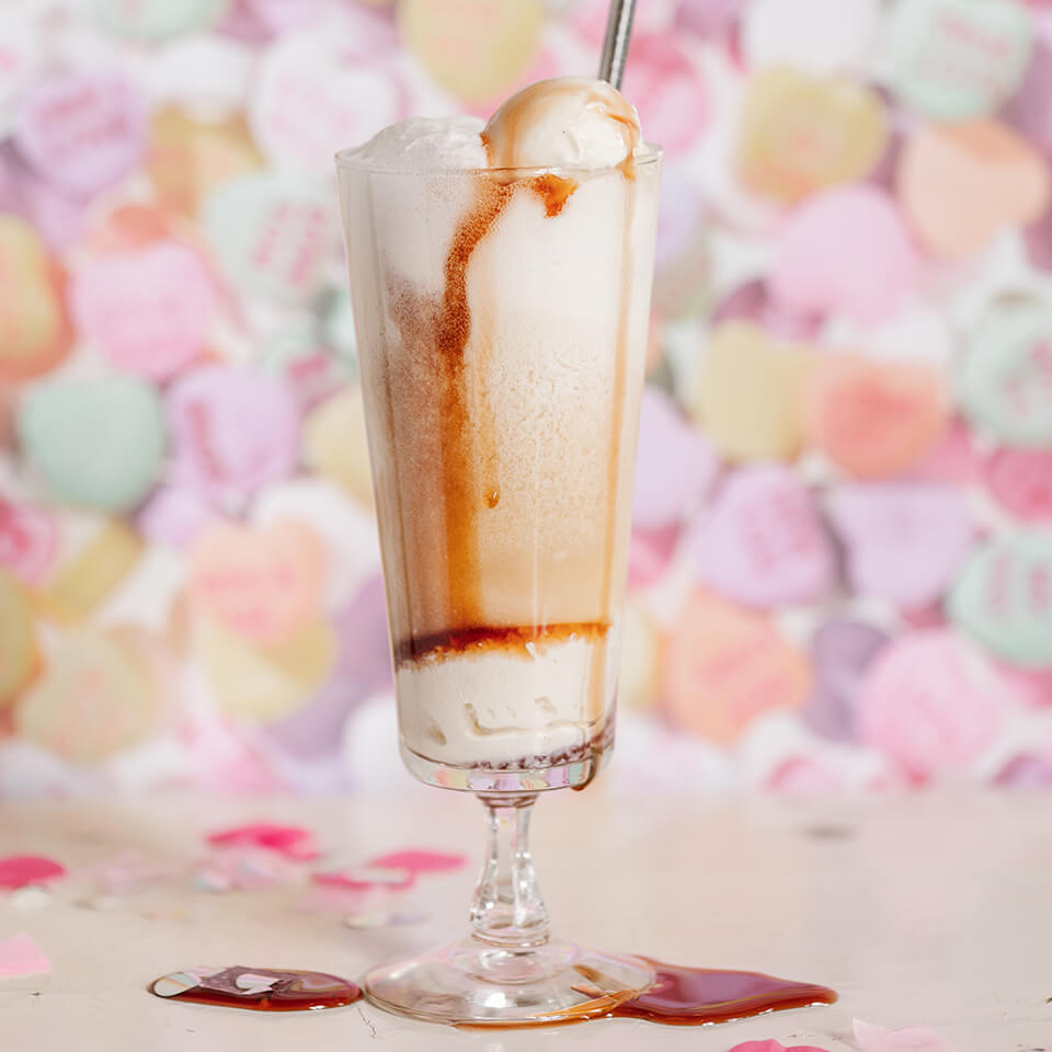 A float-style cocktail in front of a candy heart background