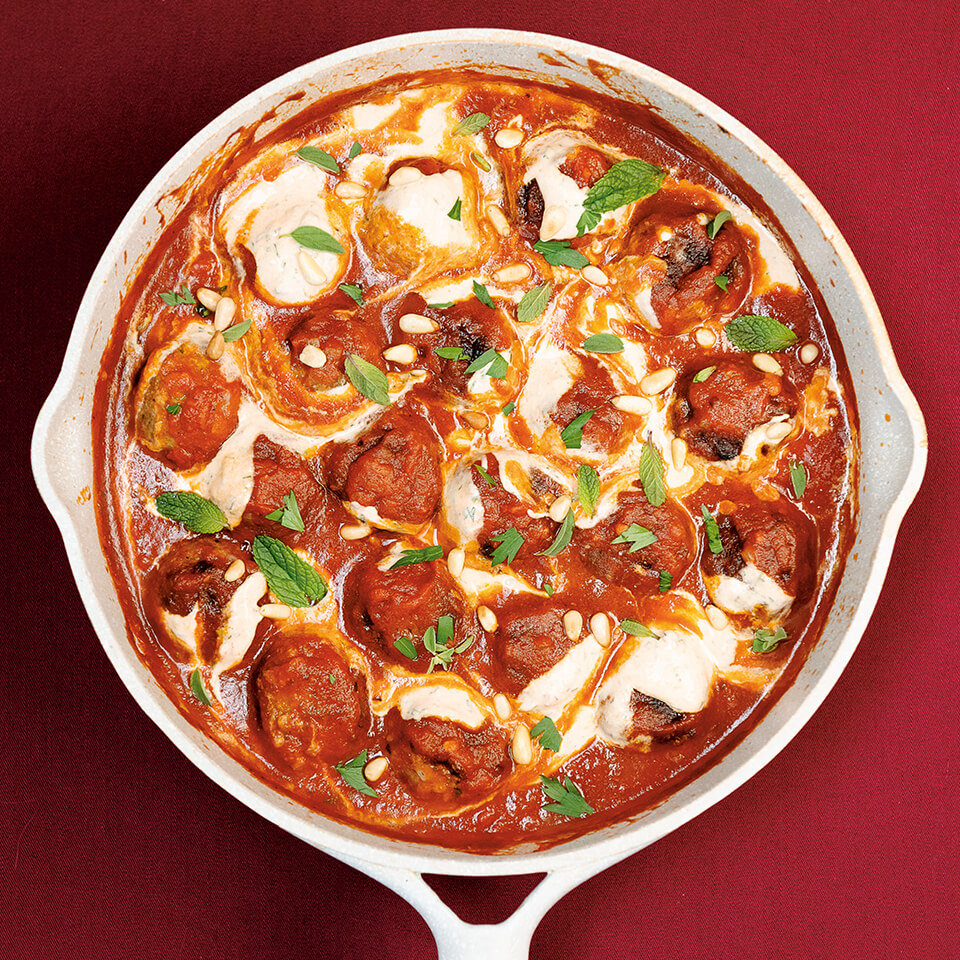 A skillet with meatballs and sauce on a red surface