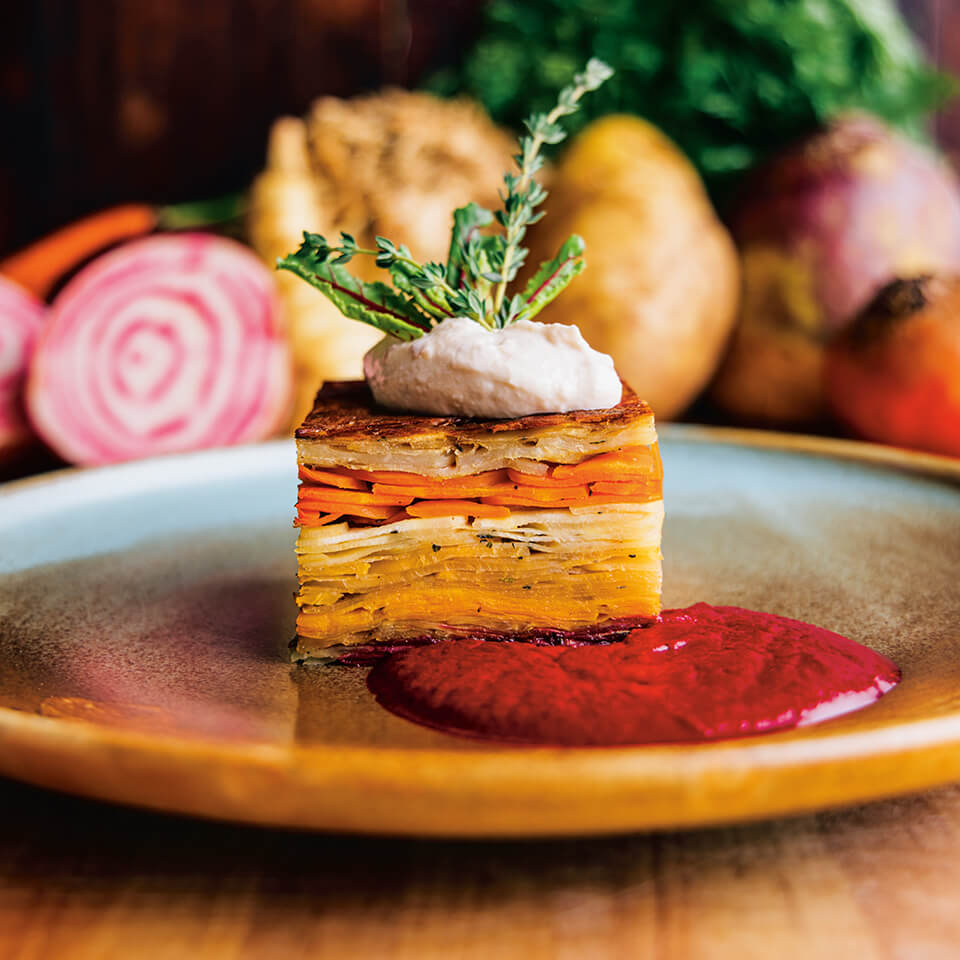 A plate with a layered root vegetable square and bright red sauce