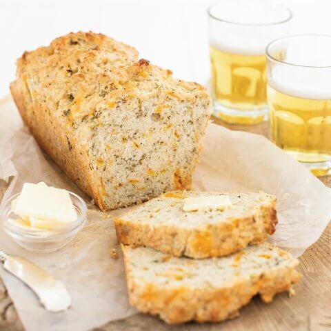 A loaf of sliced bread with glasses of beer in the background