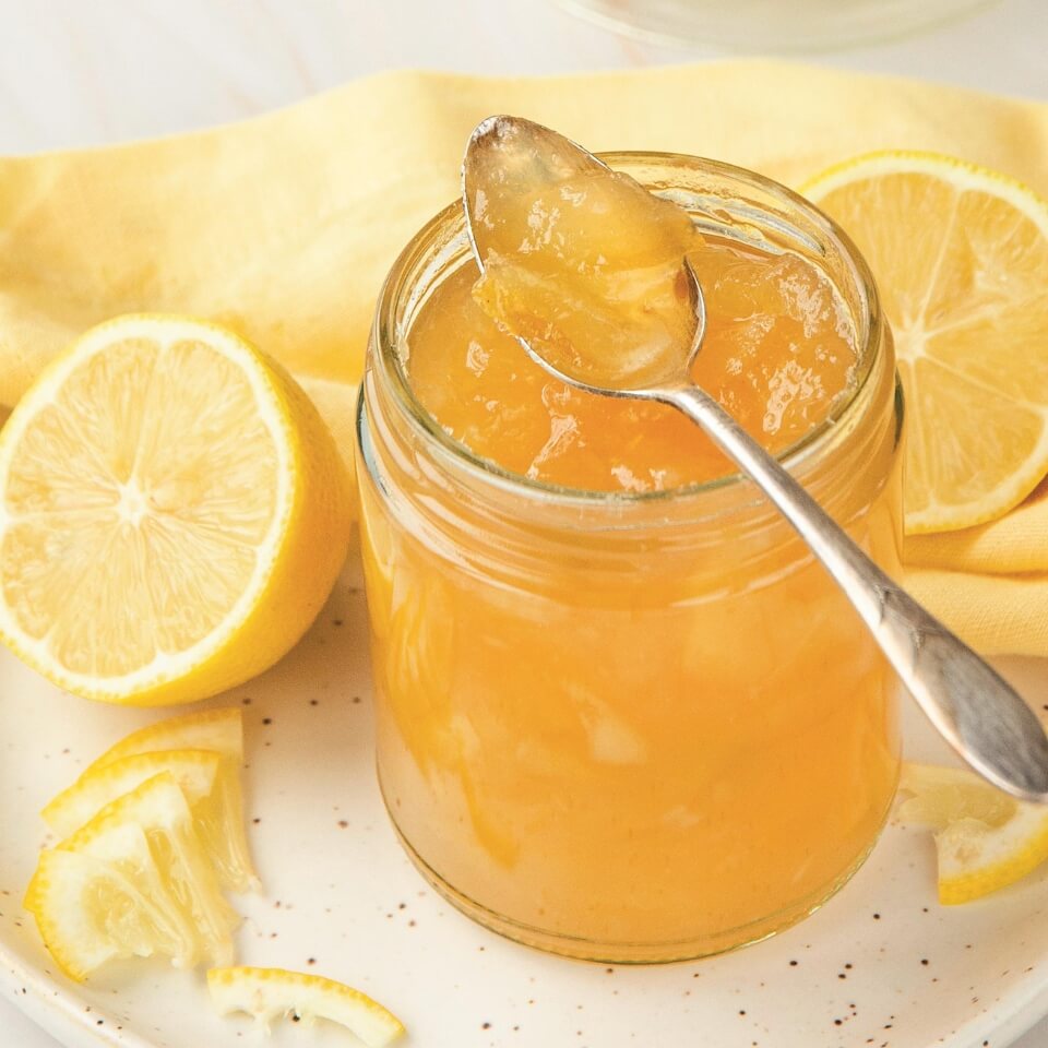 A jar of lemon marmalade with sliced lemons around it