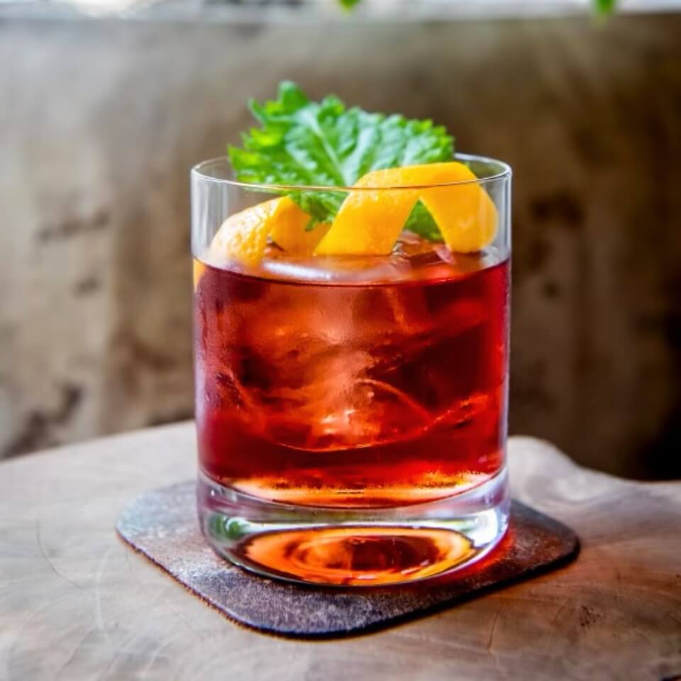 A negroni sitting on a coaster on a concrete table with a similar wall behind it