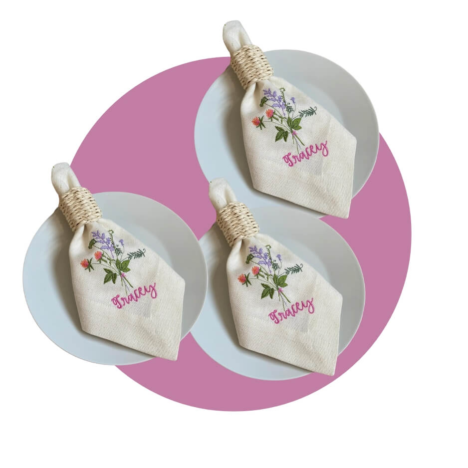 White napkins with names and flowers embroidered on them on plates over a purple cutcle