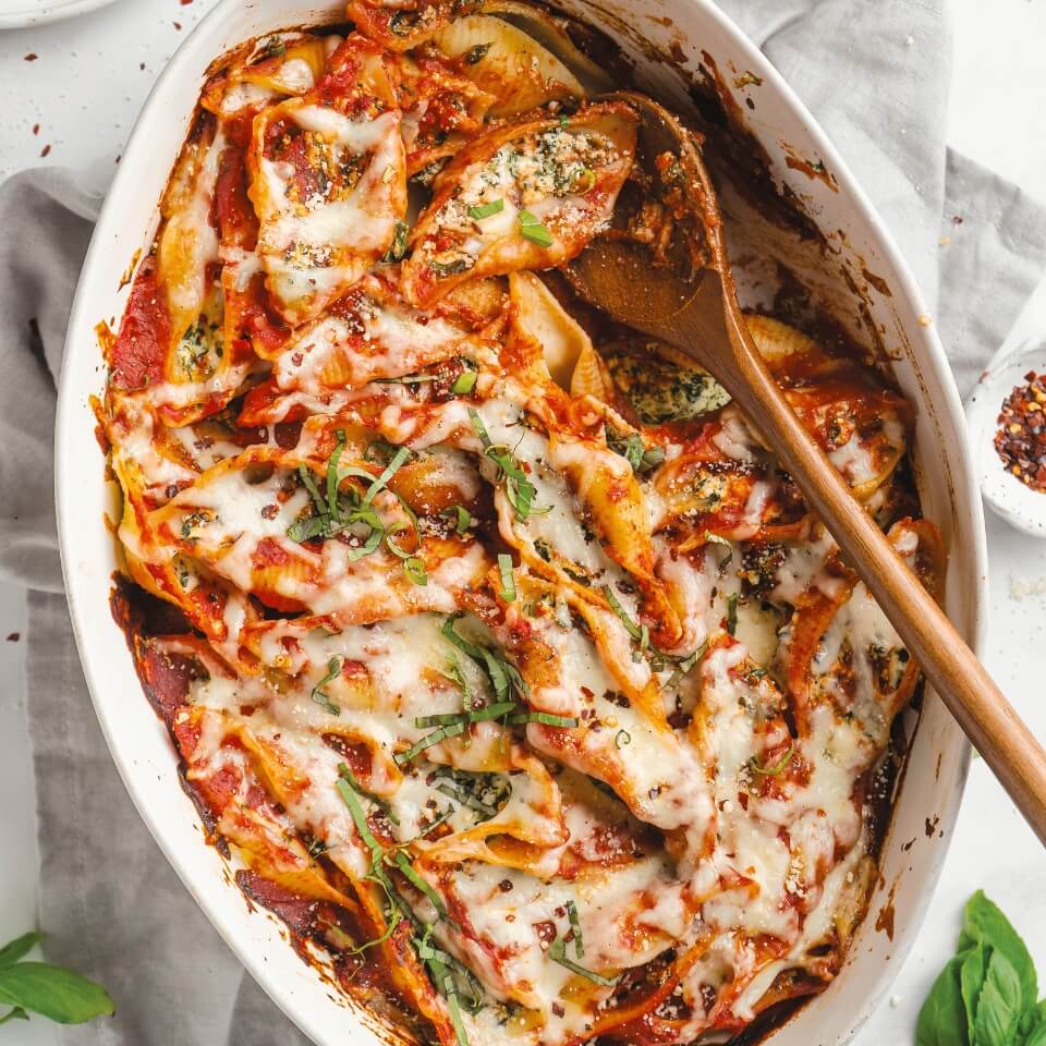 A white dish with pasta shells stuffed with spinach and ricotta in tomato sauce