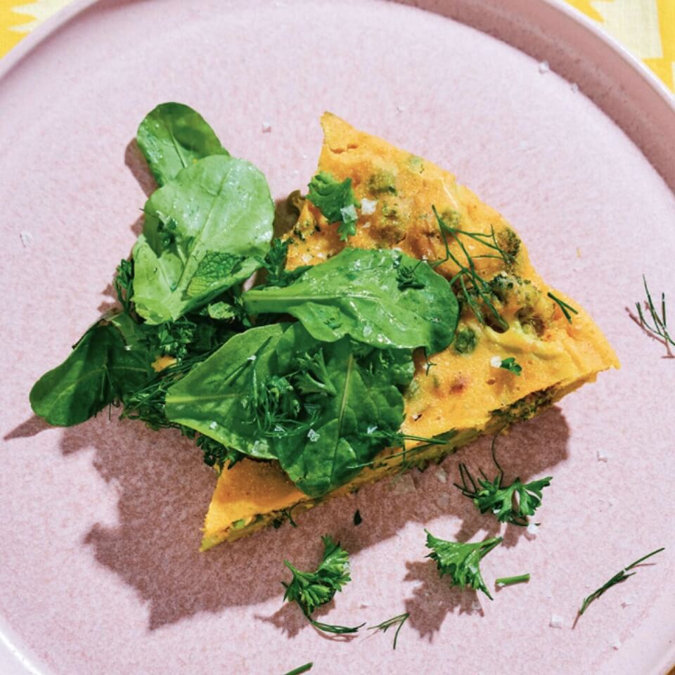 A slice of frittata topped with greens on a light purple plate