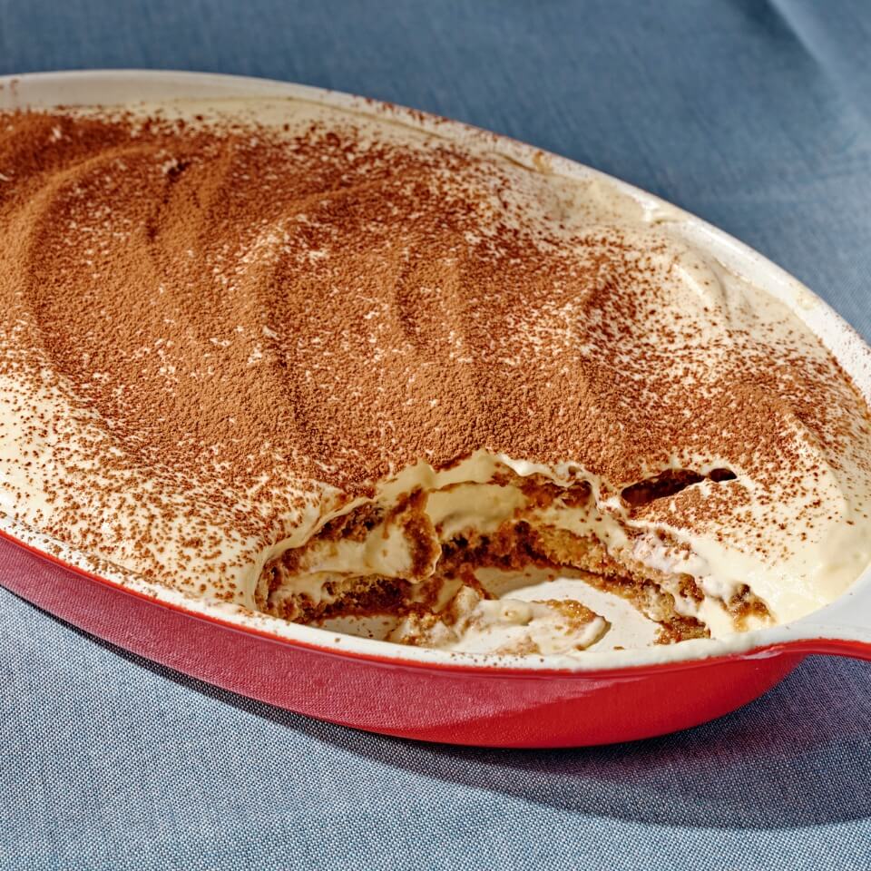 A red dish with tiramisu on a blue tablecloth