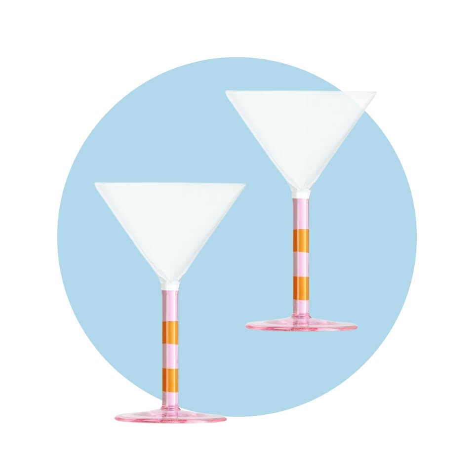 Two martini glasses with pink- and orange-striped stems over a light blue circle