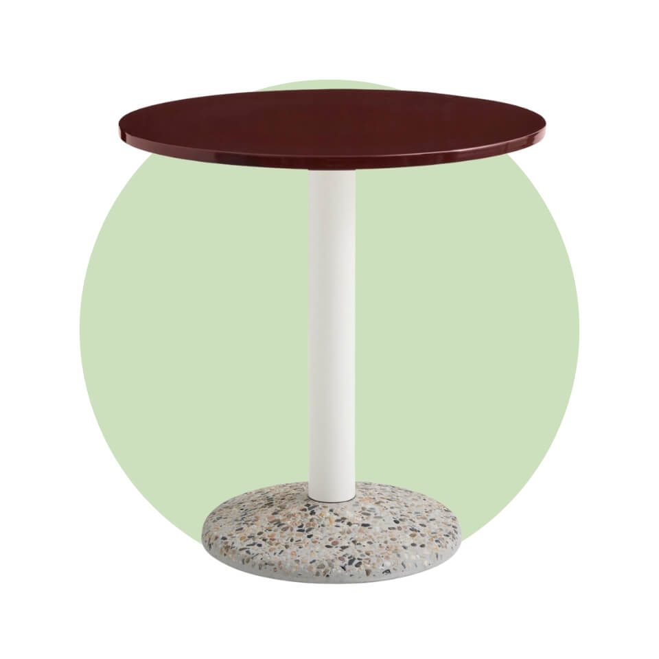 A table with a concrete base, white pole and dark red surface over a light green circle