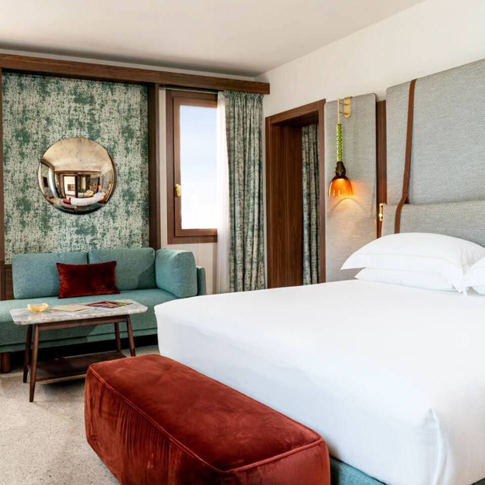 A bed in a hotel room with a blue wallpaper and a red velvet bench