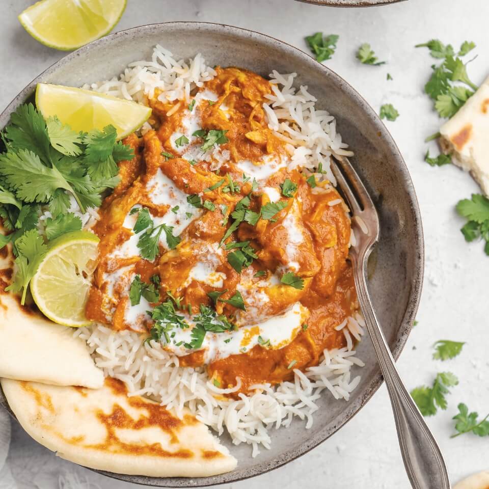 A dish of butter chicken with naan and rice