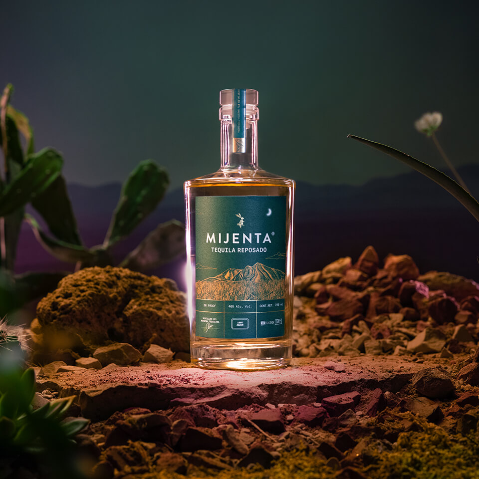 A bottle of tequila on top of a rock outside at nighttime