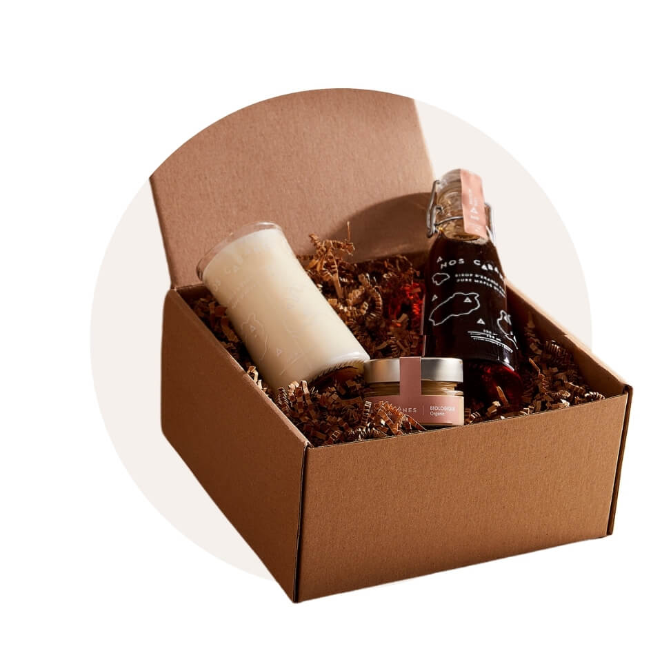 A box with a jar of maple syrup, small canister with pink label and a white candle