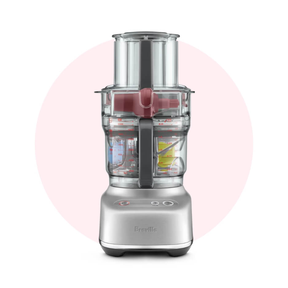 A silver food processor over a light pink circle