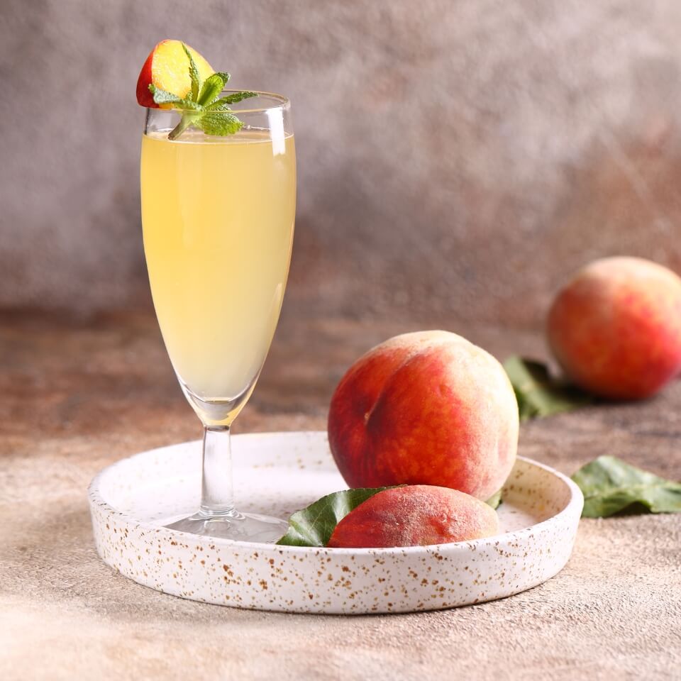 A Bellini on a small circular white plate with peaches around it