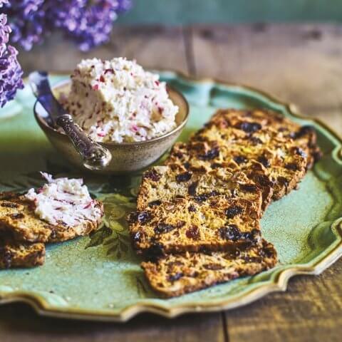 A plate with crackers and a dish of butter on a wooden table with purple flowers visible